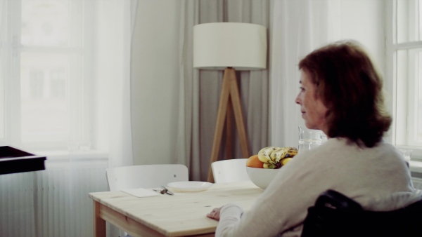 A senior couple with wheelchair sitting at the table at home, having breakfast.