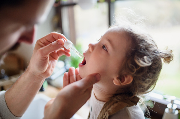 Unrecognizable father giving mouth drops to small sick daughter indoors at home.