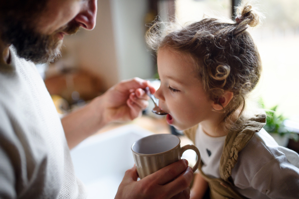 Unrecognizable mature father giving syrup to small sick daughter indoors at home.