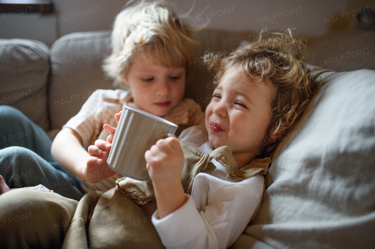 Two small sick children brother and sister at home lying in bed, drinking tea.