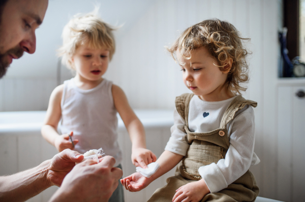 Father with children putting bandage on small hurt toddler indoors at home.