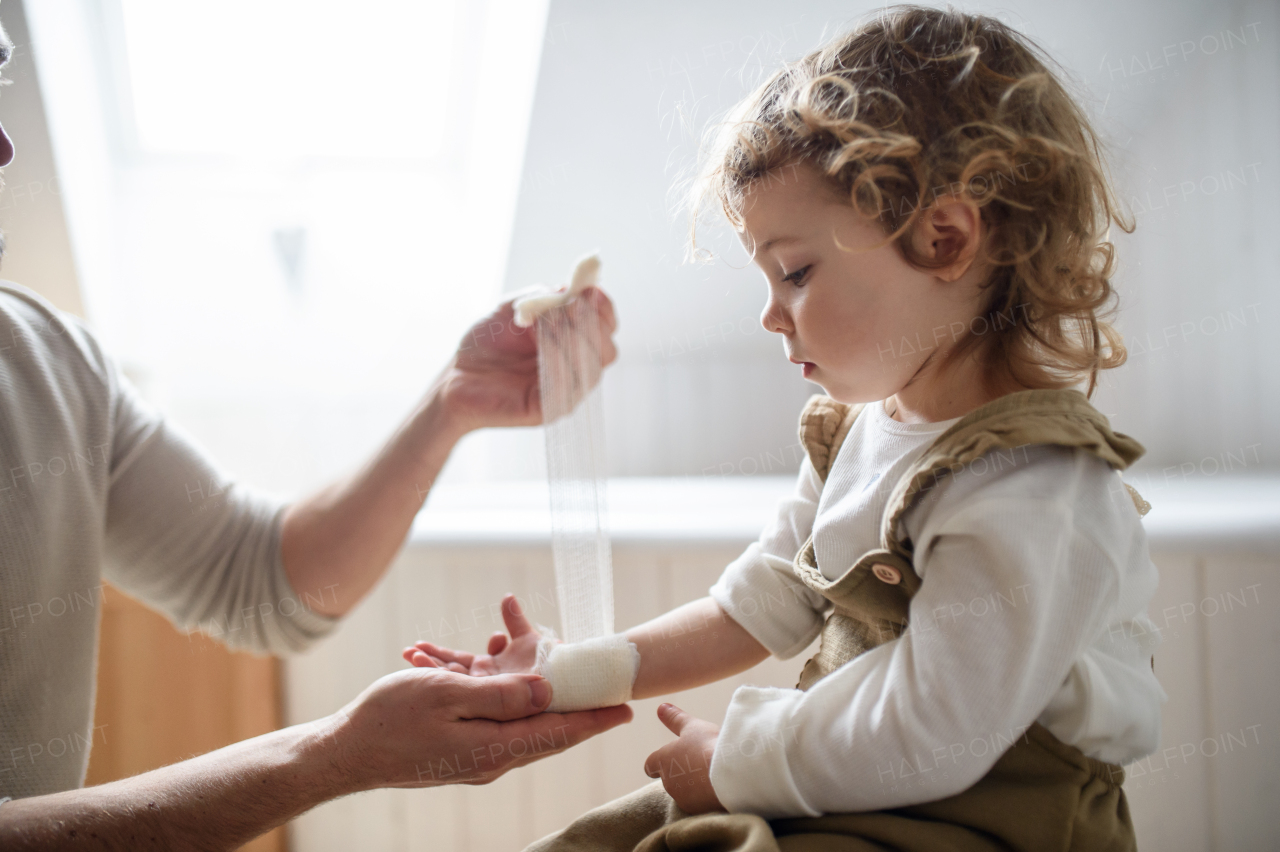 Unrecognizable father putting bandage on small hurt toddler child indoors at home.