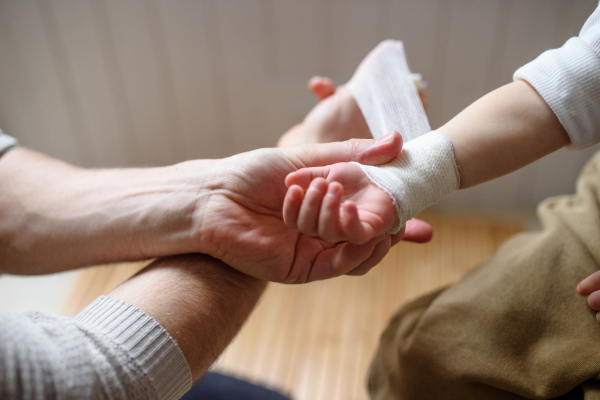 Unrecognizable father putting bandage on small hurt toddler child indoors at home.