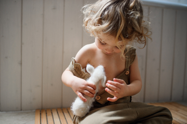 Front view of small toddler girl sitting on floor indoors at home, playing.