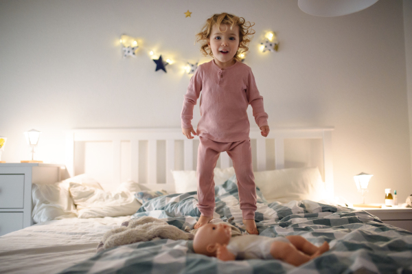 Front view of small toddler girl jumping on bed indoors at home, having fun.