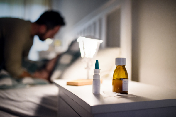 Bottle of syrup medication and nasal spray on bedsite table at home, medicine and sickness concept.