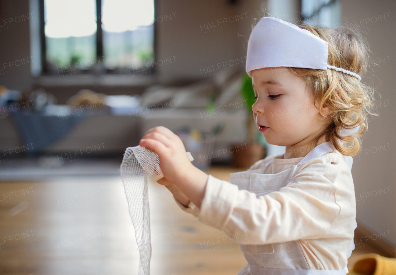 Side view of small toddler girl with doctor uniform indoors at home, playing.