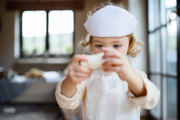 Front view of small toddler girl with doctor uniform indoors at home, playing.