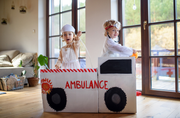 Two small children with doctor uniforms and toy ambulance car indoors at home, playing.