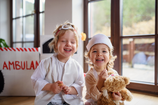 Two small children with doctor uniforms indoors at home, playing and having fun.