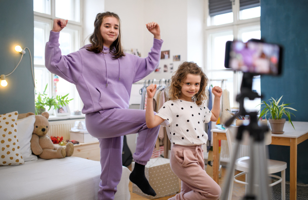 Portrait of sisters indoors at home, making video with smartphone. Lockdown concept.