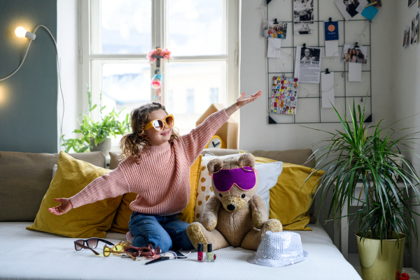 Portrait of small girl indoors at home, playing and dressing up on bed. Lockdown concept.