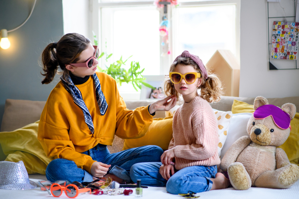 Portrait of sisters indoors at home, playing on bed. Lockdown concept.