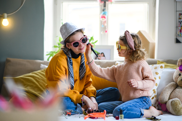 Portrait of sisters indoors at home, playing on bed. Lockdown and dressing up concept.