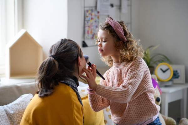 Small sisters indoors at home, applying make-up. Lockdown concept.