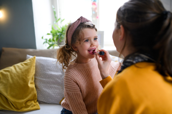 Portrait of sisters indoors at home, applying lipstick. Lockdown concept.