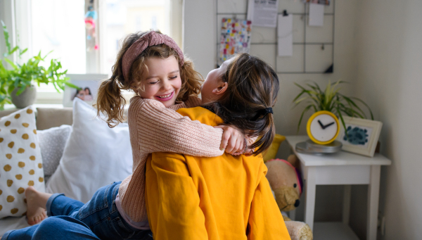 Portrait of sisters indoors at home, hugging. Lockdown concept.