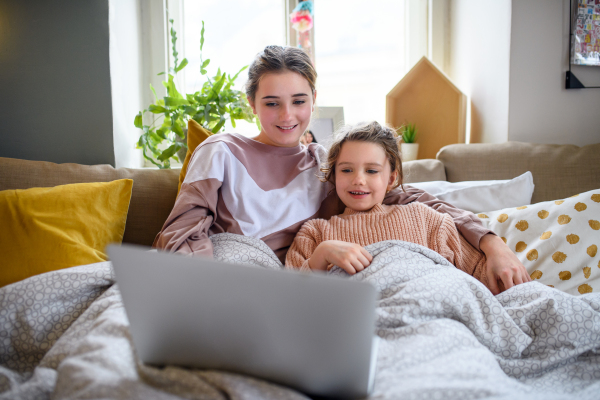 Portrait of sisters indoors at home, using laptop. Lockdown concept.