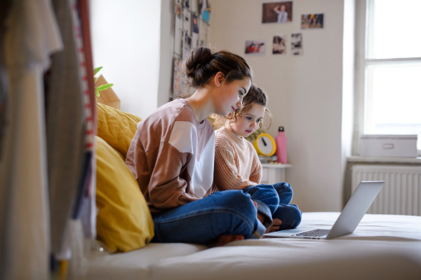 Happy sisters indoors with laptop at home, watching film. Lockdown concept.