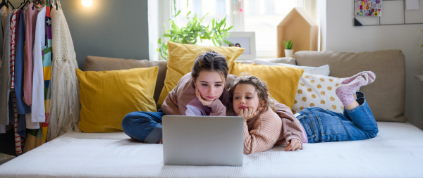 Portrait of sisters indoors at home, using laptop. Lockdown concept.