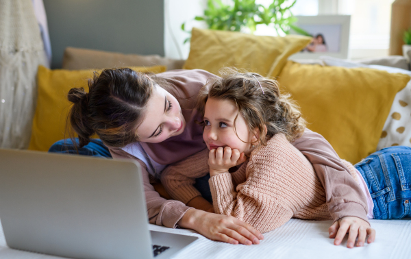 Portrait of sisters indoors at home, using laptop. Lockdown concept.