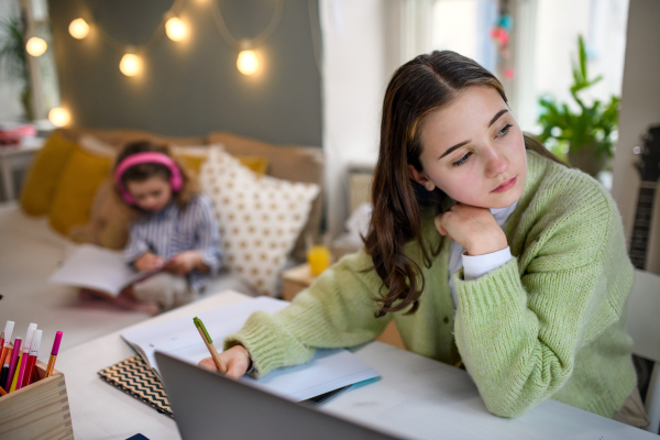 Bored teenager schoolgirl with face mask learning online indoors at home, coronavirus concept.