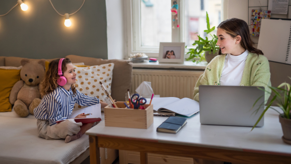 Portrait of sisters schoolgirls learning online indoors at home, coronavirus concept.