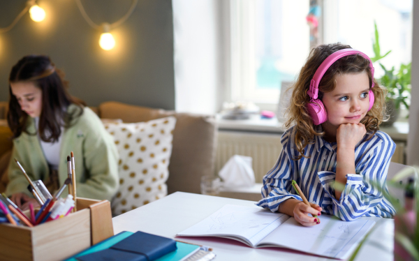 Portrait of sisters schoolgirls learning online indoors at home, coronavirus concept.