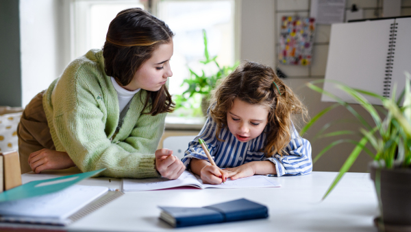 Portrait of sisters schoolgirls learning online indoors at home, coronavirus concept.