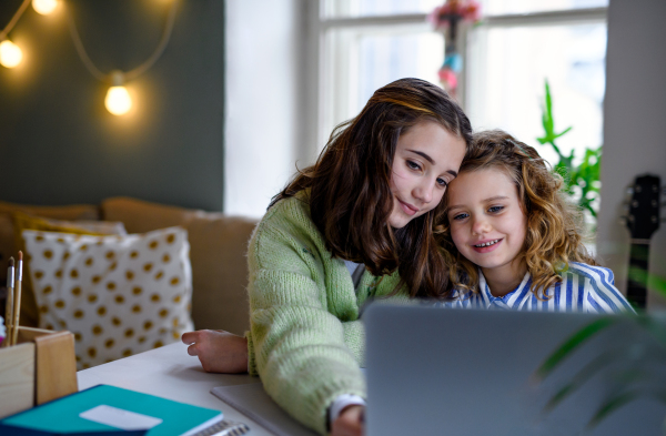 Portrait of sisters schoolgirls with laptop learning online indoors at home, coronavirus concept.