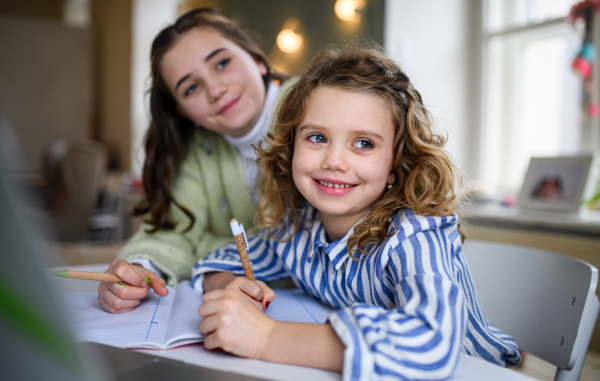 Portrait of sisters schoolgirls learning online indoors at home, coronavirus concept.