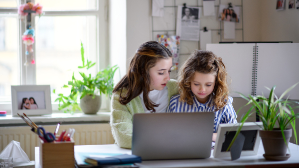 Portrait of sisters schoolgirls with laptop learning online indoors at home, coronavirus concept.