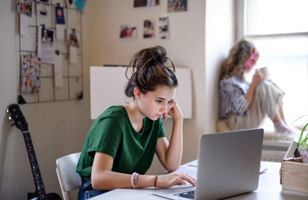 Teenager schoolgirl with face mask learning online indoors at home, coronavirus concept.