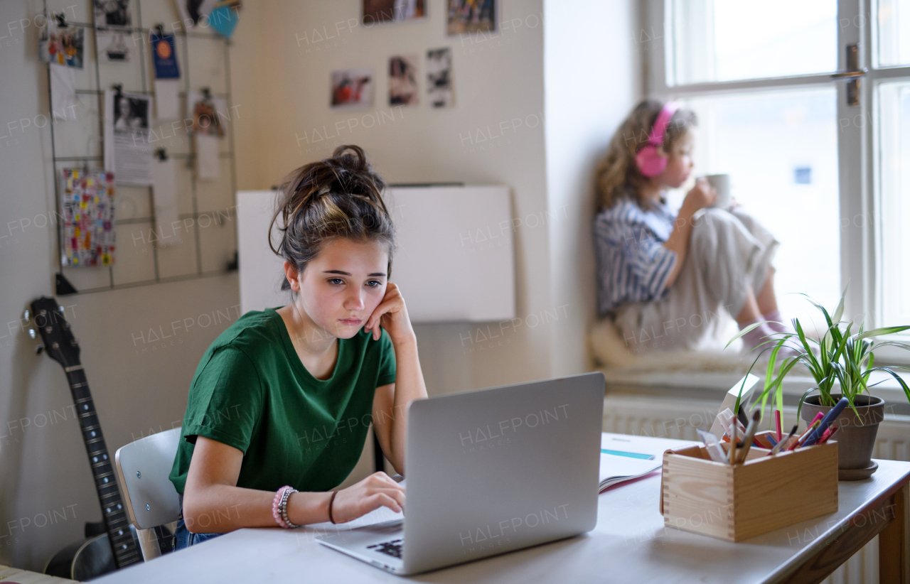 Bored teenager schoolgirl with face mask learning online indoors at home, coronavirus concept.