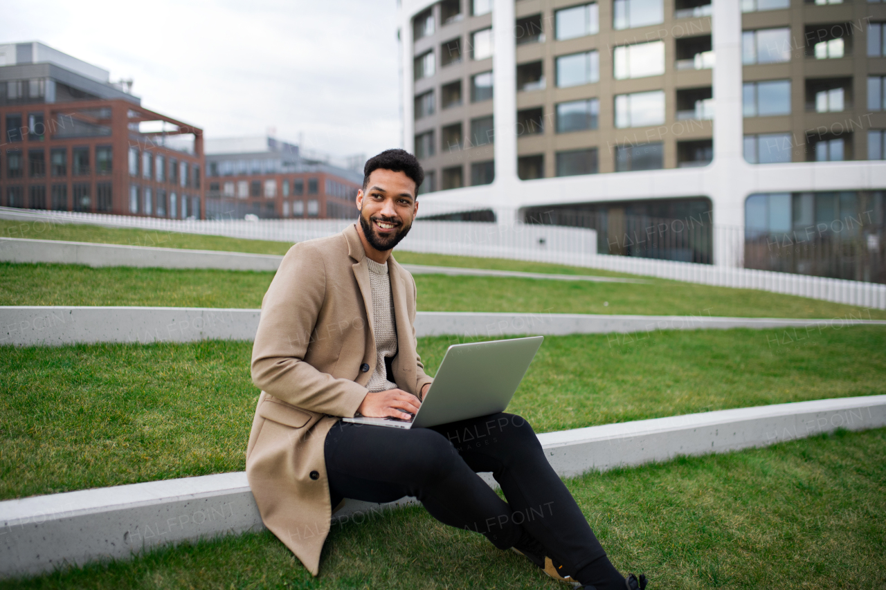 Young man with laptop working outdoors in park in city, remote office concept.