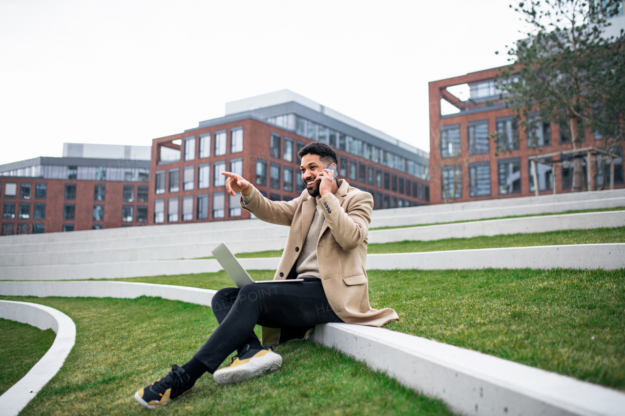 A man with laptop and smartphone outdoors in park in city, working.