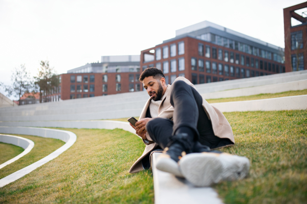 Happy man with smartphone working outdoors in park in city, resting in park.