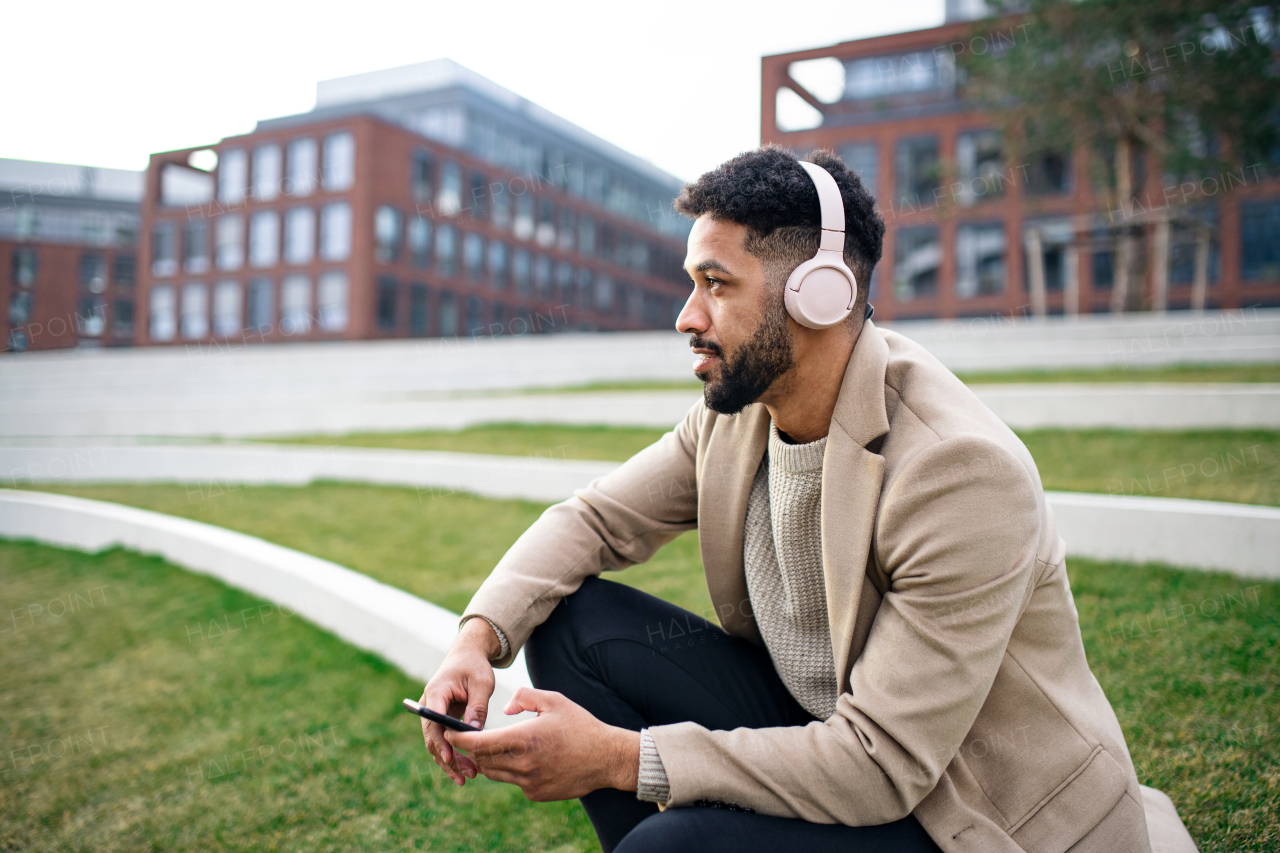 A man with headphones and martphone outdoors in park in city, resting.