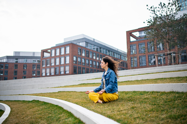 A side view portrait of woman doing yoga outdoors in park in city, eyes closed.