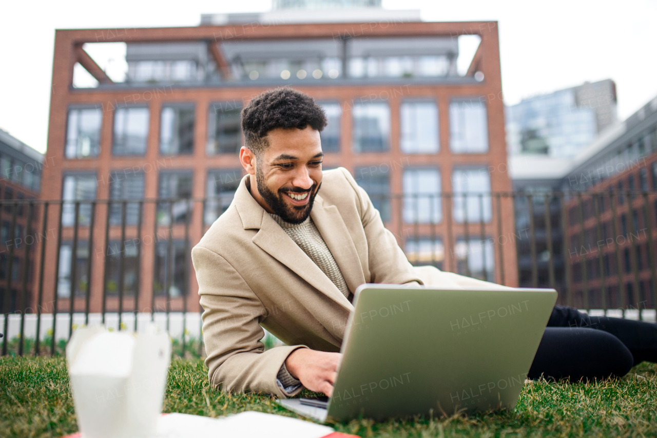 Young man with laptop working outdoors in park in city, remote office concept.