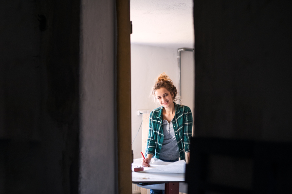 Small business of a young woman. Beautiful young woman worker in a workroom. Female carpenter sketching a project.