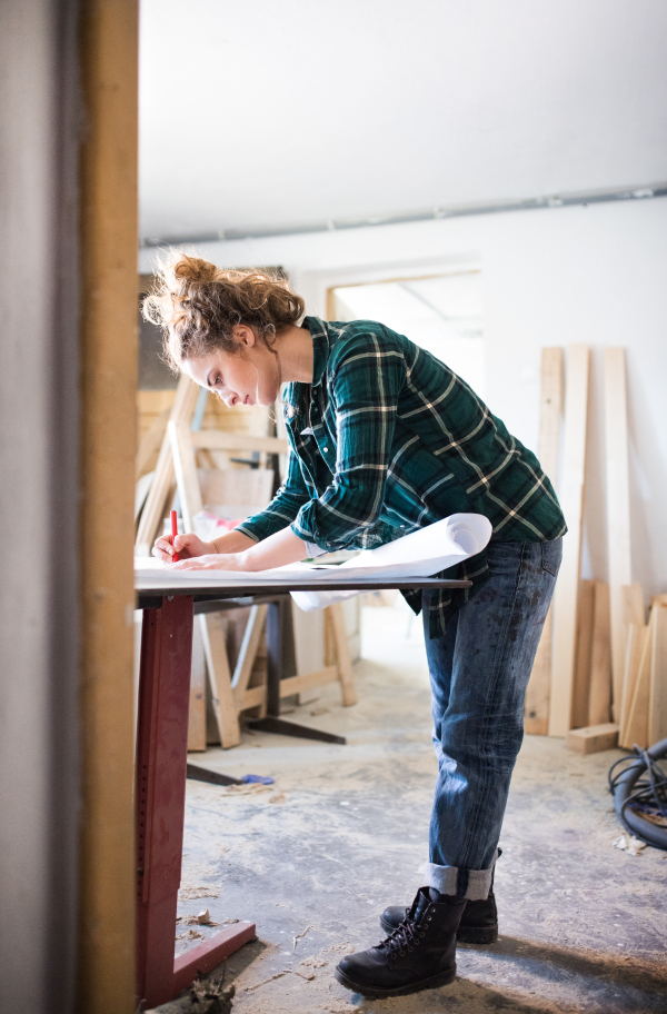 Small business of a young woman. Beautiful young woman worker in a workroom. Female carpenter sketching a project.