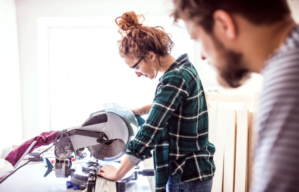 Small business of a young couple. Man and woman worker with a sander in the carpenter workroom.