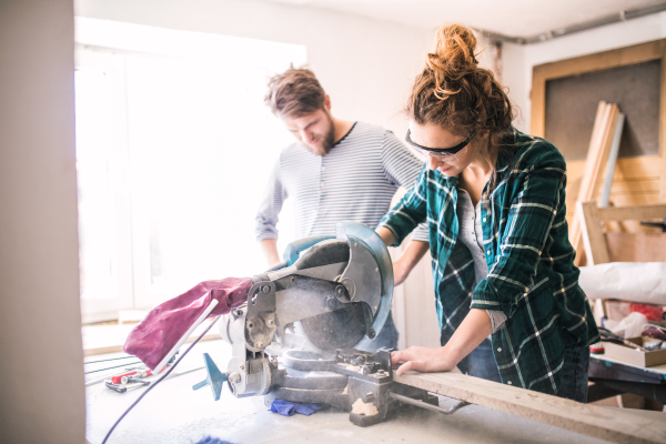 Small business of a young couple. Man and woman worker with a saw in the carpenter workroom.