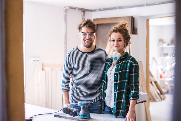 Small business of a young couple. Man and woman worker with a sander in the carpenter workroom.