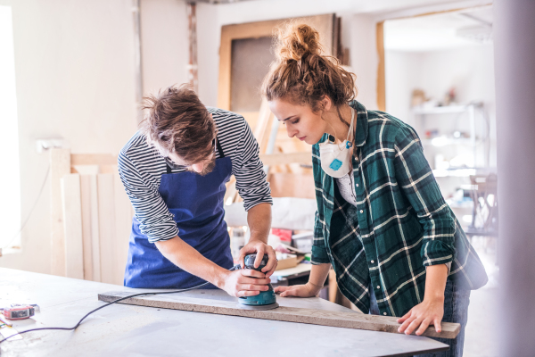 Small business of a young couple. Man and woman worker with a sander in the carpenter workroom.