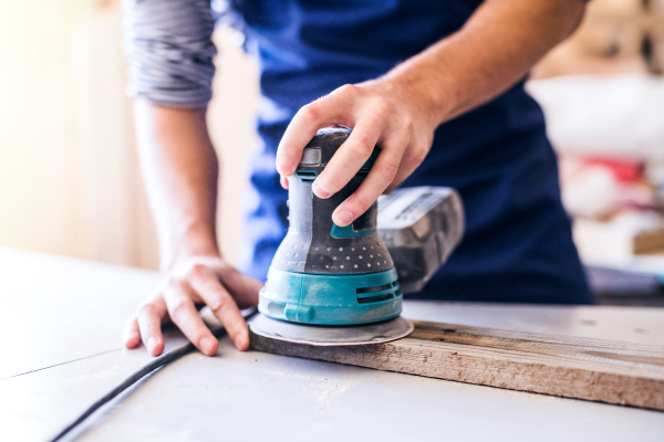 Small business of a young man. Unrecognizable worker with a sander in the carpenter workroom.