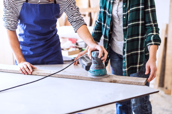 Small business of a young couple. Unrecognizable man and woman worker with a sander in the carpenter workroom.