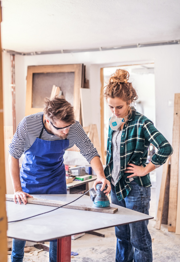 Small business of a young couple. Man and woman worker with a sander in the carpenter workroom.