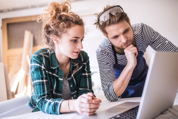 Man and woman worker with laptop in the carpenter workroom. Young couple working together.